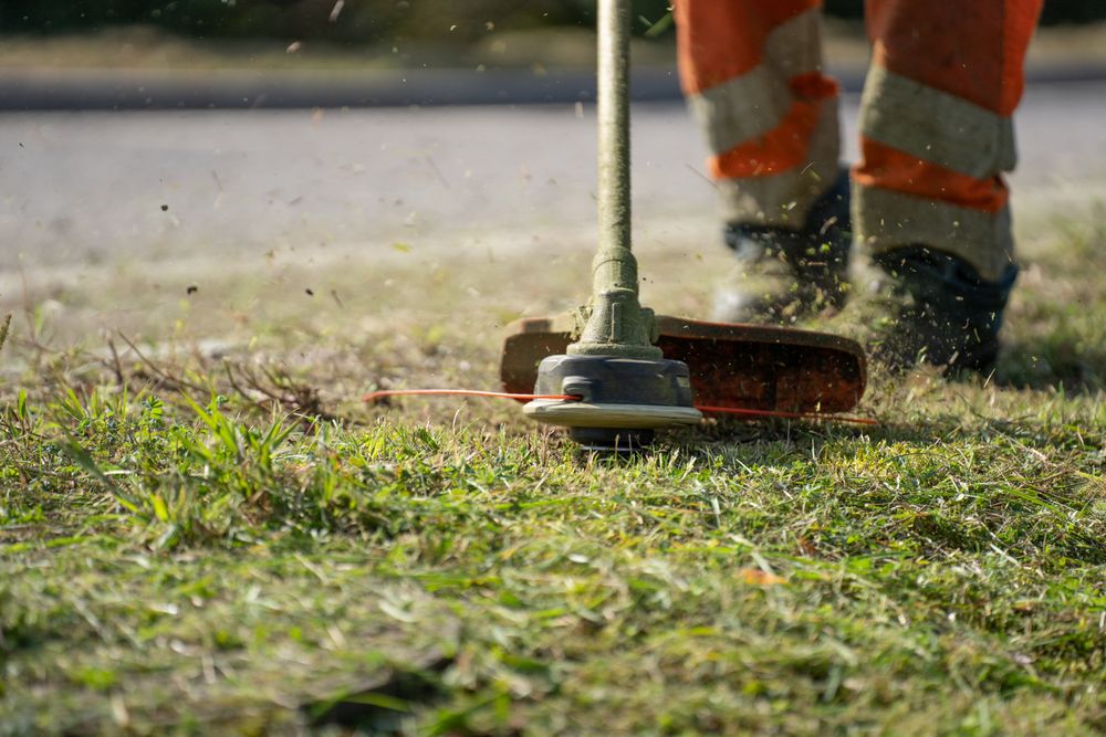 A grounds worker trimming grass beside a hard surface